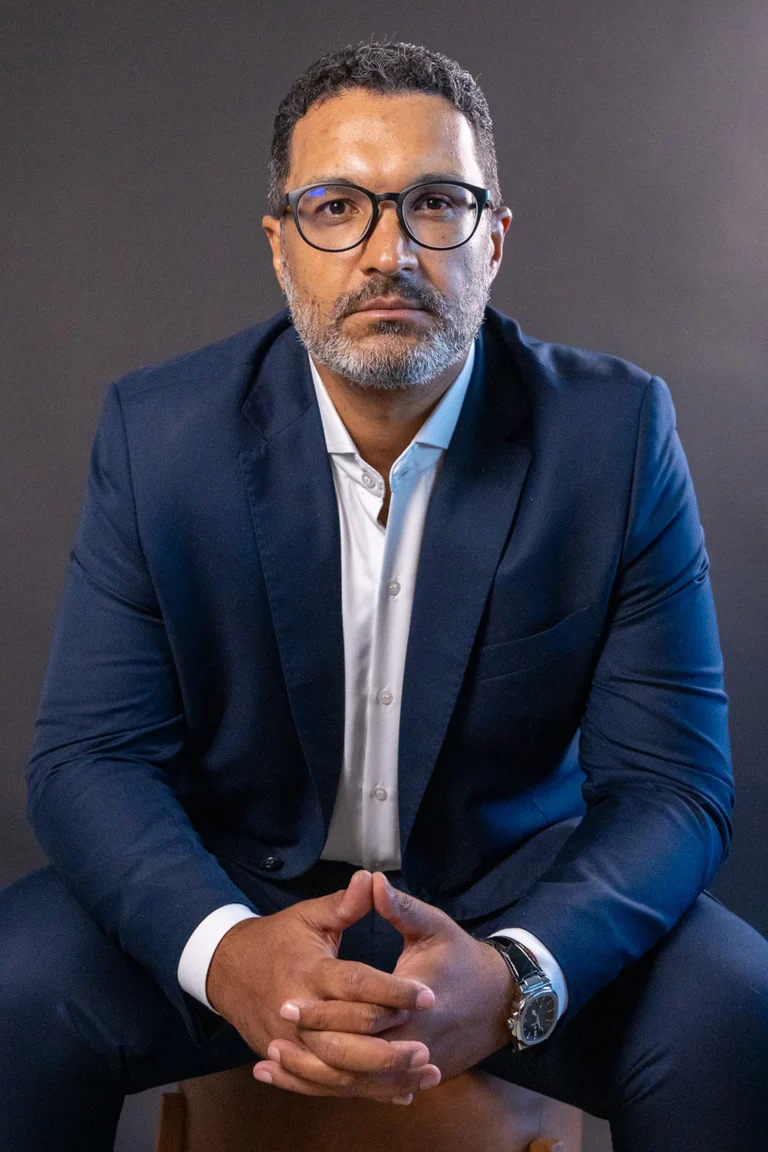 Watson Silva sentado, de terno azul, com as mãos entrelaçadas